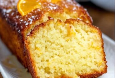 Orange glaze pound cake on a wire rack with white glaze drizzled down the sides, golden buttery loaf cake with tight crumb, fresh orange zest on top, slice cut showing moist interior