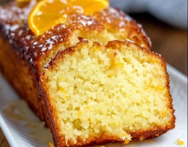 Orange glaze pound cake on a wire rack with white glaze drizzled down the sides, golden buttery loaf cake with tight crumb, fresh orange zest on top, slice cut showing moist interior