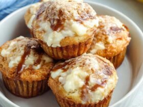 Banana cream cheese muffins on a wooden board, golden banana muffins with visible white cream cheese centers, sliced banana slices on top, sprinkle of brown sugar