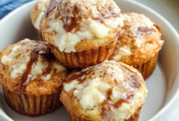 Banana cream cheese muffins on a wooden board, golden banana muffins with visible white cream cheese centers, sliced banana slices on top, sprinkle of brown sugar