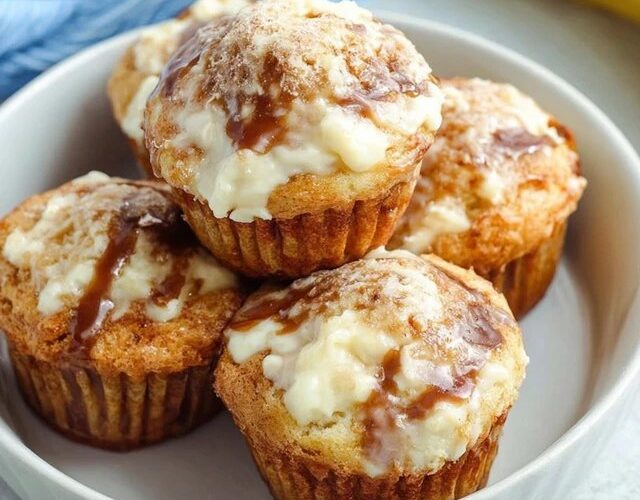 Banana cream cheese muffins on a wooden board, golden banana muffins with visible white cream cheese centers, sliced banana slices on top, sprinkle of brown sugar