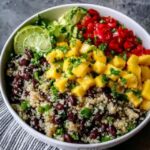 Quinoa black bean mango salad in a large serving bowl, fluffy white quinoa, black beans, bright orange mango cubes, red bell pepper, red onion, fresh cilantro, lime wedges, drizzle of dressing on top, summery natural light
