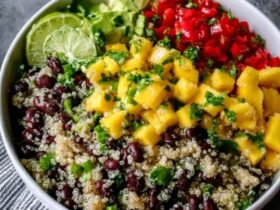Quinoa black bean mango salad in a large serving bowl, fluffy white quinoa, black beans, bright orange mango cubes, red bell pepper, red onion, fresh cilantro, lime wedges, drizzle of dressing on top, summery natural light