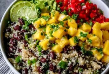 Quinoa black bean mango salad in a large serving bowl, fluffy white quinoa, black beans, bright orange mango cubes, red bell pepper, red onion, fresh cilantro, lime wedges, drizzle of dressing on top, summery natural light