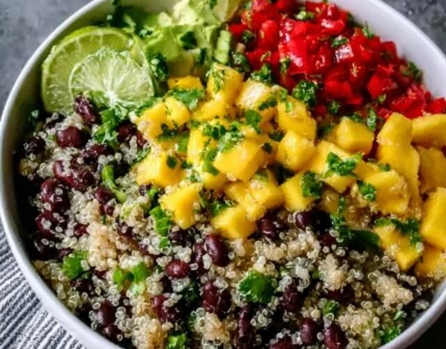 Quinoa black bean mango salad in a large serving bowl, fluffy white quinoa, black beans, bright orange mango cubes, red bell pepper, red onion, fresh cilantro, lime wedges, drizzle of dressing on top, summery natural light