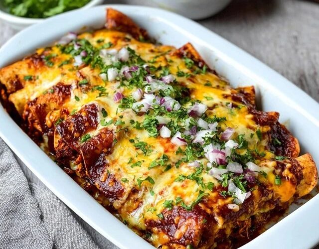 Cheese enchiladas in a casserole dish, rolled corn tortillas covered in deep red enchilada sauce and melted cheese, fresh cilantro, diced red onion on top, sour cream dollops, lime wedges, served in a Mexican ceramic dish