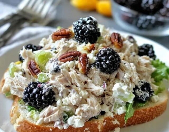 Chicken salad sandwich on toasted croissant, creamy chunky chicken salad with halved red grapes, celery and herbs spilling out, lettuce leaf, served with chips on the side