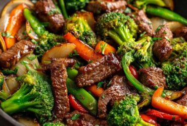 Beef and broccoli stir fry in a wok, glossy dark brown sauce coating tender beef strips and bright green broccoli florets, sesame seeds and sliced green onion on top, served over white rice