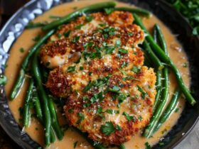 Parmesan crusted chicken overhead on a plate with green beans, golden crispy parmesan-panko crust, juicy chicken, fresh parsley and lemon wedge, dish fills the frame, warm golden tones