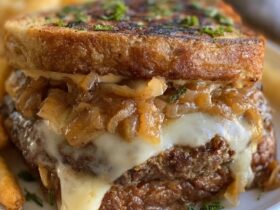 French onion burger on a toasted bun, juicy beef patty smothered in deeply caramelized onions and melted gruyere cheese, with a side of fries