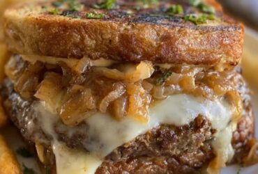 French onion burger on a toasted bun, juicy beef patty smothered in deeply caramelized onions and melted gruyere cheese, with a side of fries