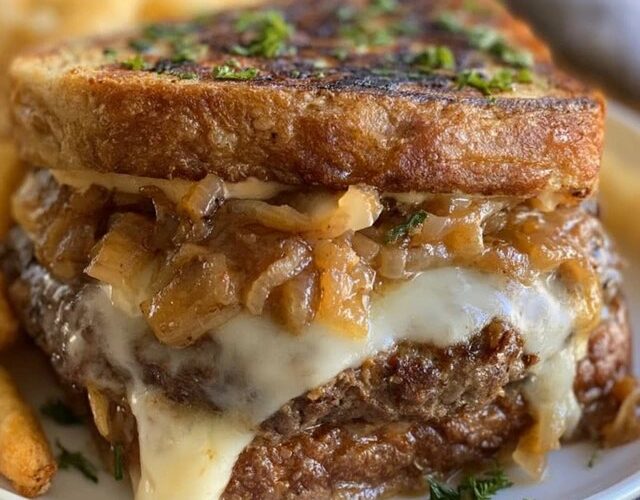 French onion burger on a toasted bun, juicy beef patty smothered in deeply caramelized onions and melted gruyere cheese, with a side of fries