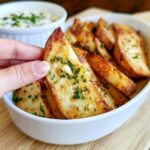 Garlic parmesan potato wedges on a baking sheet, crispy golden wedges coated in parmesan, garlic and herbs, garnished with parsley, a bowl of garlic aioli for dipping