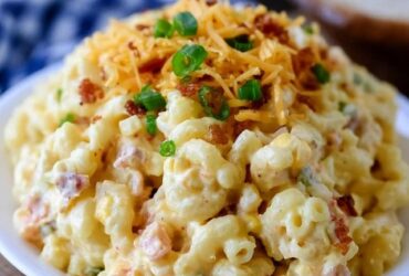 Cheesy bacon macaroni salad in a bowl, elbow macaroni in a creamy dressing with cubes of cheddar, crispy bacon bits, diced celery and red onion, sprinkle of chives