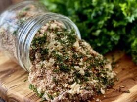 Homemade herb and spice blend in a small glass jar and spilled on a spoon, a rich brown-red seasoning mix with visible dried herbs, paprika and pepper flakes