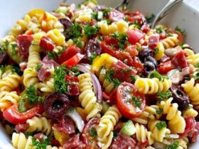 Italian pasta salad in a big bowl, rotini with salami, mozzarella balls, cherry tomatoes, bell peppers, olives and red onion in Italian dressing, parsley on top