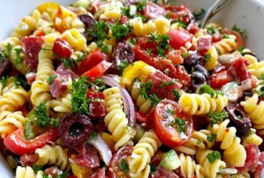 Italian pasta salad in a big bowl, rotini with salami, mozzarella balls, cherry tomatoes, bell peppers, olives and red onion in Italian dressing, parsley on top