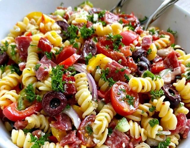 Italian pasta salad in a big bowl, rotini with salami, mozzarella balls, cherry tomatoes, bell peppers, olives and red onion in Italian dressing, parsley on top