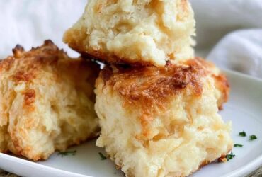 Cheddar bay biscuits piled on a plate, golden fluffy biscuits flecked with cheddar, brushed with garlic herb butter and sprinkled with parsley