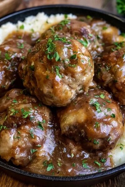 Meatballs and mashed potatoes on a plate, juicy browned beef meatballs smothered in rich brown gravy over a mound of creamy mashed potatoes, parsley garnish