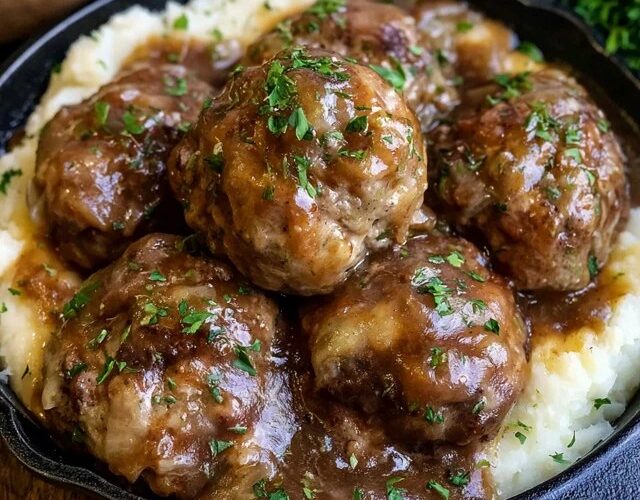 Meatballs and mashed potatoes on a plate, juicy browned beef meatballs smothered in rich brown gravy over a mound of creamy mashed potatoes, parsley garnish